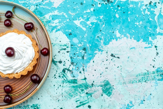 Draufsicht auf cupcake mit sauerkirschen und sahne auf hellblau und weiß,