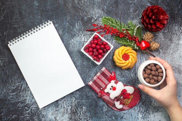 Draufsicht auf das köstliche Biskuit-Dekorationszubehör des Notebooks Weihnachtssocke und Cornell in einer Schüssel Tannenzweige auf dunkler Oberfläche