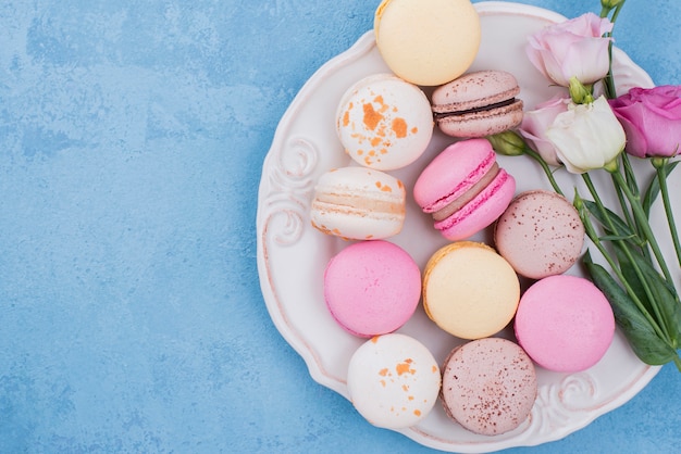 Draufsicht auf das sortiment von macarons auf teller mit rosen