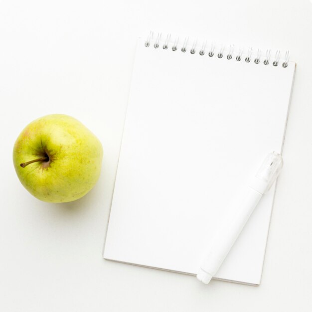 Draufsicht auf das Wesentliche des Schulanfangs mit Apfel und Notizbuch