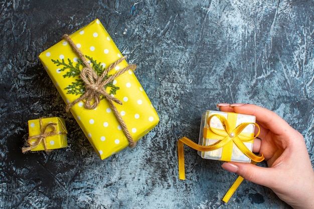 Draufsicht auf die hand, die eine kleine geschenkbox und zwei andere weihnachtsgeschenkboxen auf dunklem hintergrund hält