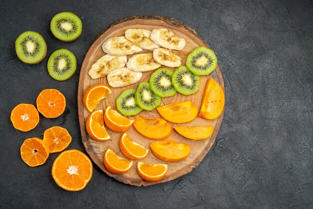 Draufsicht auf die Hand, die eine Orangenscheibe aus einem natürlichen organischen frischen Obst auf dem Schneidebrett und um sie herum auf dunklem Hintergrund nimmt