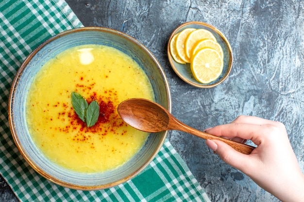 Draufsicht auf die Hand mit einem Löffel und einem blauen Topf mit leckerer Suppe, serviert mit Minze und Pfeffer min