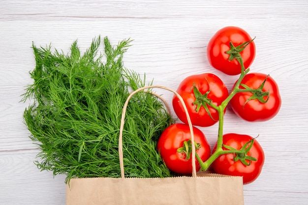 Draufsicht auf ein Bündel Frühlingszwiebeln in einem Korb und Tomaten mit Stiel auf weißem Hintergrund