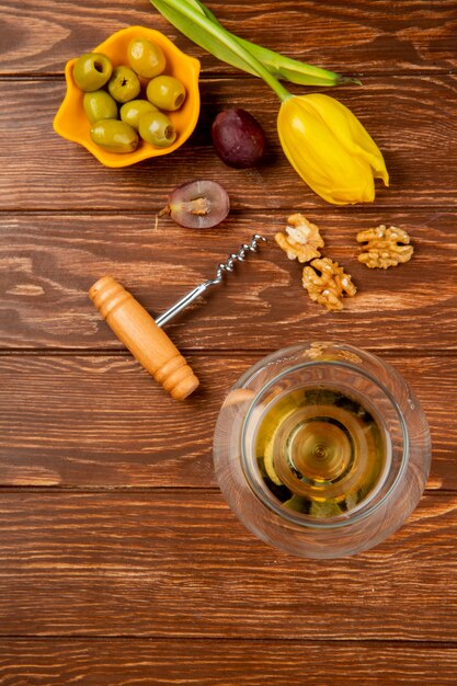 Draufsicht auf ein Glas Weißwein mit Korkenzieher der Oliven-Walnuss-Traube und Blume auf Holztisch