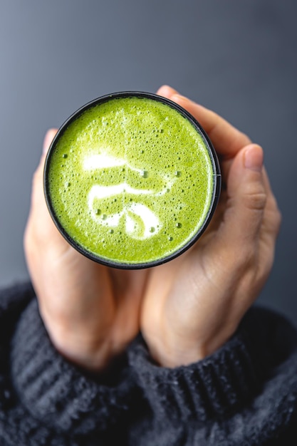 Kostenloses Foto draufsicht auf eine frau, die ein trendiges grünes matcha-getränk mit latte art in den händen hält