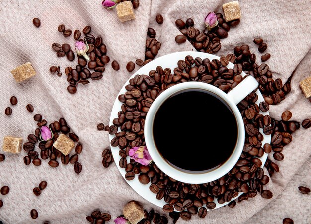 Draufsicht auf eine Tasse Kaffee mit braunen Zuckerwürfeln der Kaffeebohnen und Teerosenknospen