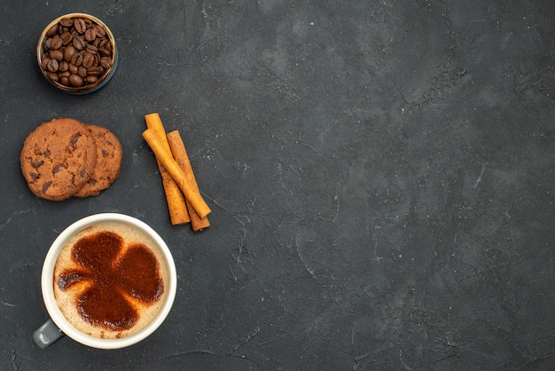 Draufsicht auf eine Tasse Kaffee mit Kaffeebohnensamen, Zimtstangen und Keksen auf dunklem, isoliertem Hintergrund