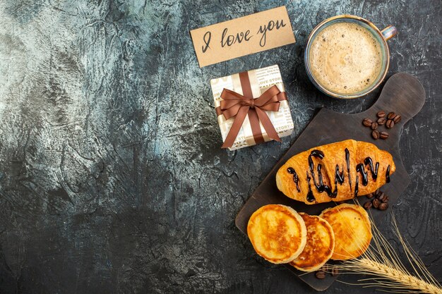Draufsicht auf eine Tasse Kaffee und frisches leckeres Frühstück schöne Geschenkbox Pfannkuchen Croisasant auf dunklem Hintergrund