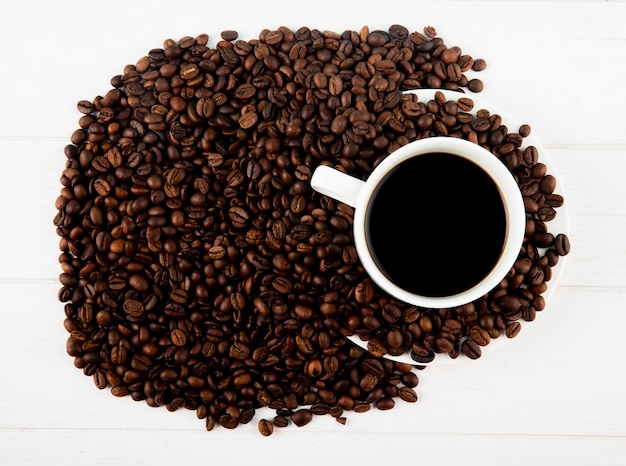 Draufsicht auf eine Tasse Kaffee und Kaffeebohnen verstreut auf weißem Hintergrund