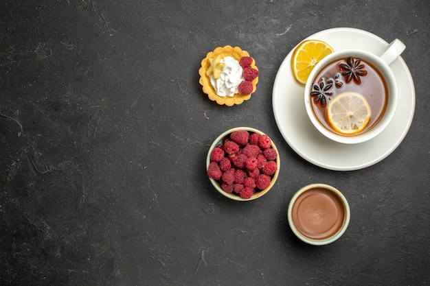 Draufsicht auf eine Tasse schwarzen Tee mit Zitrone, serviert mit Schokoladen-Himbeer-Honig auf dunklem Hintergrund