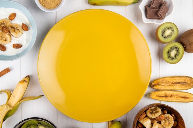 Draufsicht auf einen gelben Teller und frische Bananen- und Kiwifrüchte, die auf Weiß angeordnet sind
