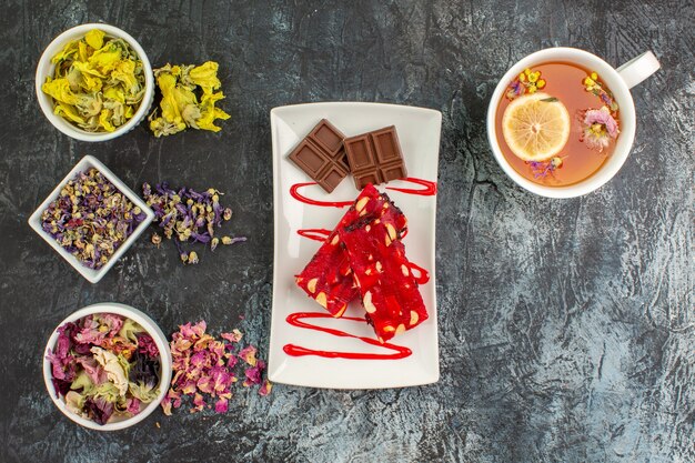 Draufsicht auf einen Schokoladenteller mit einer Tasse Kräutertee und Schalen mit trockenen Blumen auf grauem Grund