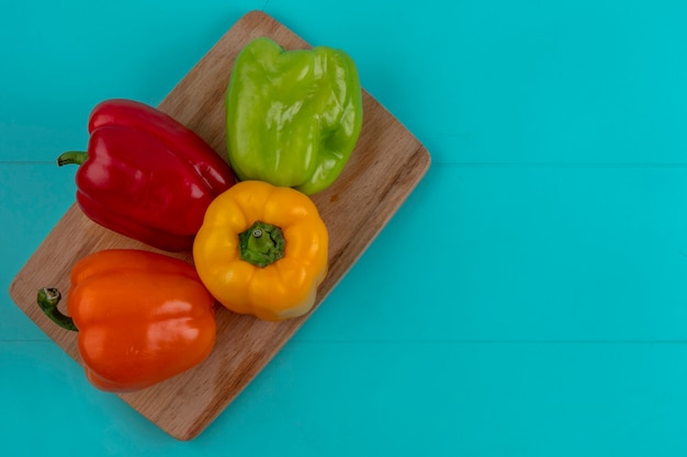 Draufsicht auf farbige Paprika auf einem Schneidebrett auf einer türkisfarbenen Oberfläche