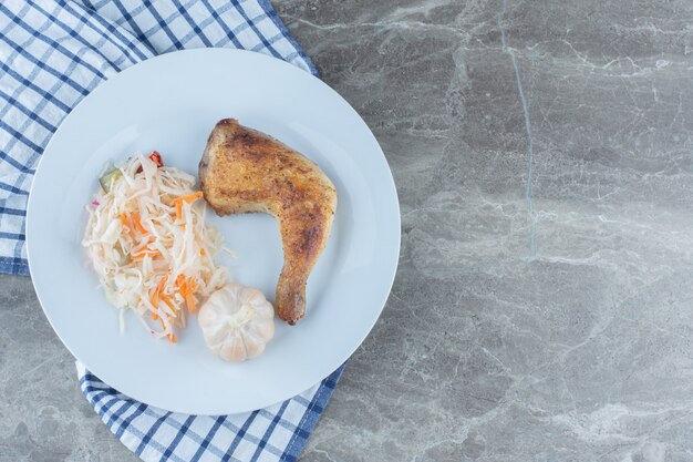 Draufsicht auf frisch gegrilltes Hühnerbein und Sauerkraut auf weißem Teller.