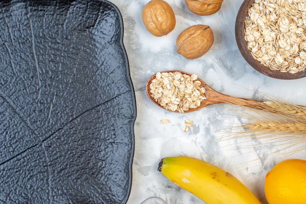 Draufsicht auf frische Bananen-Holzlöffel-Wanuts-Hafer in einem braunen Topf und schwarzem Tablett auf Eishintergrund