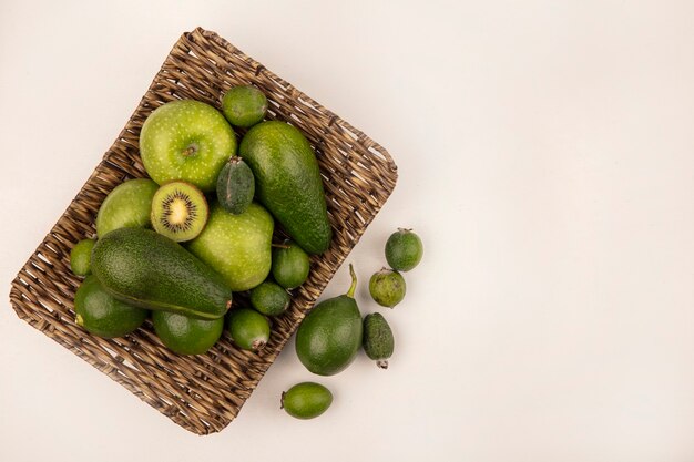 Draufsicht auf frische Früchte wie grüne Apfel-Feijoas-Avocados auf einem Weidentablett auf einer weißen Wand mit Kopierraum