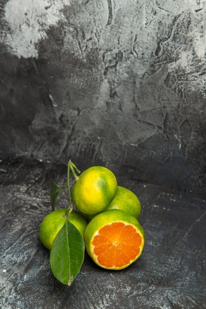 Draufsicht auf frische ganze grüne Mandarinen mit Blättern und einer halben Mandarine auf grauem Hintergrundmaterial