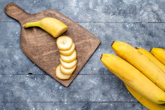Draufsicht auf frische gelbe Bananen geschnitten und ganz auf graue, frische Fruchtbeere