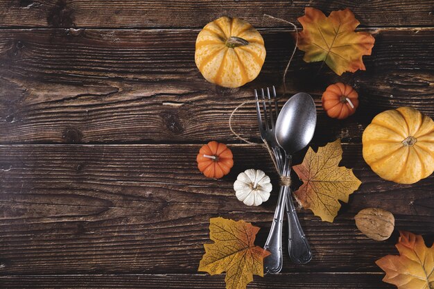 Draufsicht auf frische Kürbisse, Walnüsse, Herbstblätter mit Gabel und Löffel auf einem Holztisch