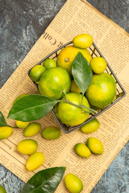 Draufsicht auf frische Kumquats und Zitronen in einem schwarzen Korb auf Zeitungen auf grauem Hintergrund stockbild