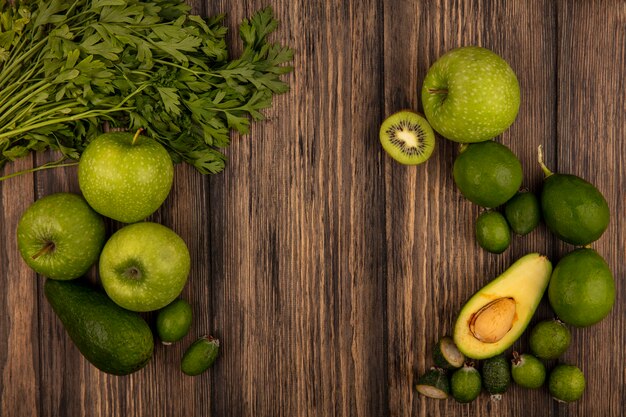 Draufsicht auf frische Lebensmittel wie grüne Äpfel, Limetten, Feijoas, Avocados und Petersilie, isoliert auf einer Holzwand mit Kopierraum