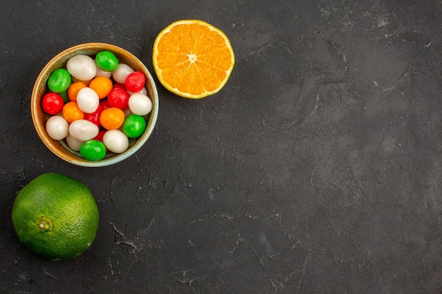 Draufsicht auf frische Mandarinen mit bunten Bonbons auf schwarzem Tisch