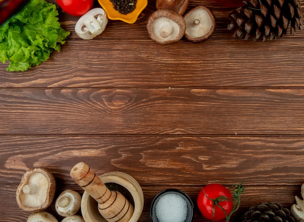 Draufsicht auf frische Pilze mit frischem Tomatenholzmörser der schwarzen Pfefferkörner mit getrocknetem Kräutersalz und Zapfen auf rustikalem Holz mit Kopierraum