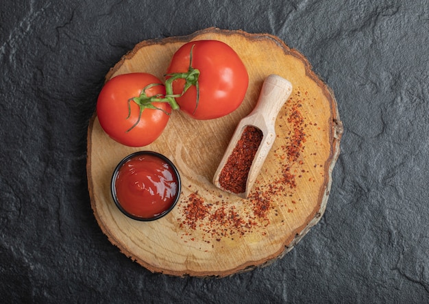 Draufsicht auf frische reife Tomaten mit Ketchup und Pfeffer auf Holzbrett auf schwarzem Hintergrund.