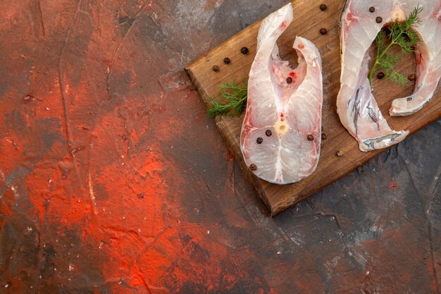 Draufsicht auf frische rohe Fische und Pfeffer auf Holzschneidebrett auf der linken Seite auf Mischfarboberfläche