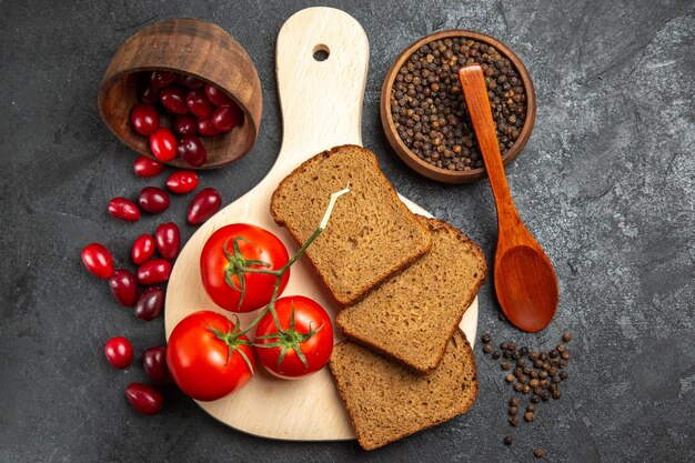 Draufsicht auf frische rote Hartriegel mit Brotlaib und Tomaten auf grauer Oberfläche