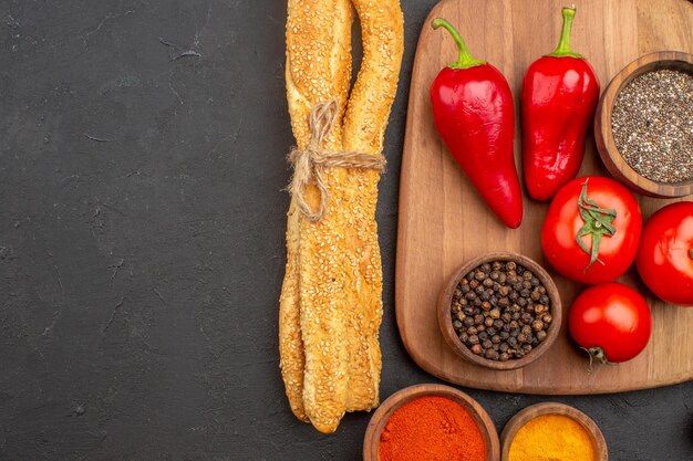 Draufsicht auf frische rote Tomaten mit Brot und Gewürzen auf Schwarz