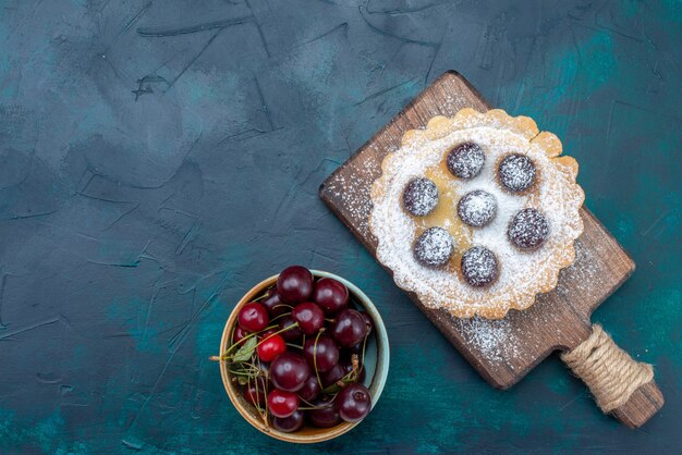 Draufsicht auf frische Sauerkirschen mit rundem Kuchen auf dunklem Schreibtisch, Obstkuchen-Kekszuckersüß