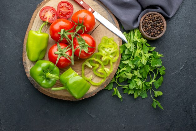 Draufsicht auf frische Tomaten und grüne Paprikaschoten auf grünem Holzbrettbündel auf schwarzer Oberfläche