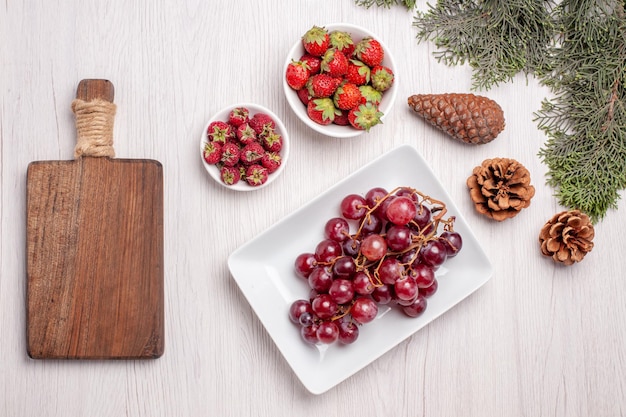 Draufsicht auf frische Trauben mit Erdbeeren und Himbeeren auf weißem Tisch