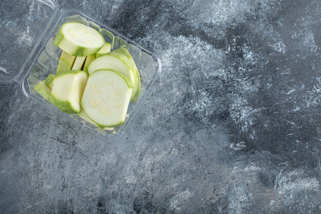 Draufsicht auf frische Zucchinistücke im Plastikbehälter.