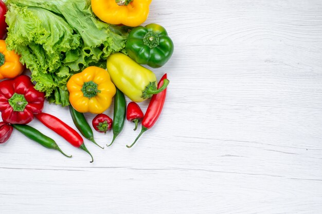 Draufsicht auf frischen grünen Salat zusammen mit Paprika und würzigen Paprikaschoten auf leichtem Schreibtisch, Zutat für Gemüsemahlzeiten