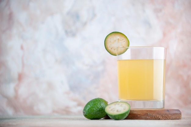 Draufsicht auf frischen saft und goldenen löffel halbierte ganze feijoas auf kleinem holzbrett auf der linken seite auf pastellfarbenem hintergrund