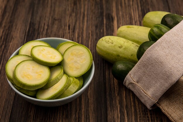 Draufsicht auf frisches Gemüse wie Gurken und Zucchini auf einem Leinensack mit gehackten Zucchini auf einer Schüssel auf einer Holzwand