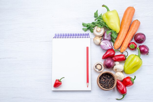 Draufsicht auf frisches Gemüse wie Pfeffer-Karotten-Zwiebeln auf leichtem Schreibtisch, Gemüsemahlzeit-Vitamin