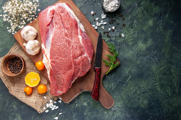 Draufsicht auf frisches rohes rotes Fleisch, grüne Knoblauchzehen auf braunem Holzbrett Tomatenpfeffer auf nacktem Handtuchmesser auf dunklem Hintergrund