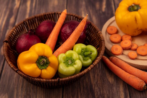 Draufsicht auf frisches und gesundes Gemüse wie bunte Paprika und Karotten der roten Zwiebeln auf einem Eimer auf einer Holzoberfläche