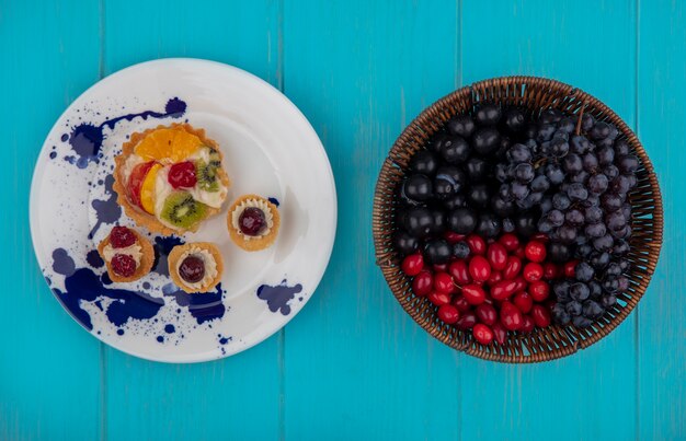 Draufsicht auf fruchtige Cupcakes in Teller und Früchten als Cornel Sloe Beeren und Trauben auf blauem Hintergrund