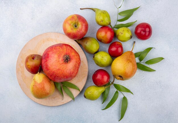 Draufsicht auf Früchte als Pflaumenpfirsich und Granatapfel auf Schneidebrett und mit Apfel auf weißer Oberfläche