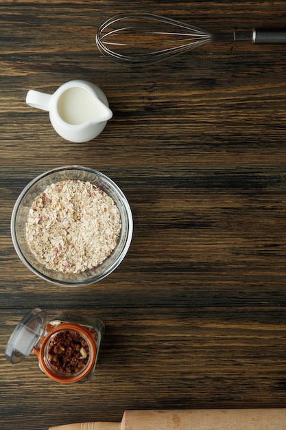 Draufsicht auf Frühstückszutaten wie Hafer-Walnuss-Milch mit Schneebesen und Nudelholz auf Holzhintergrund