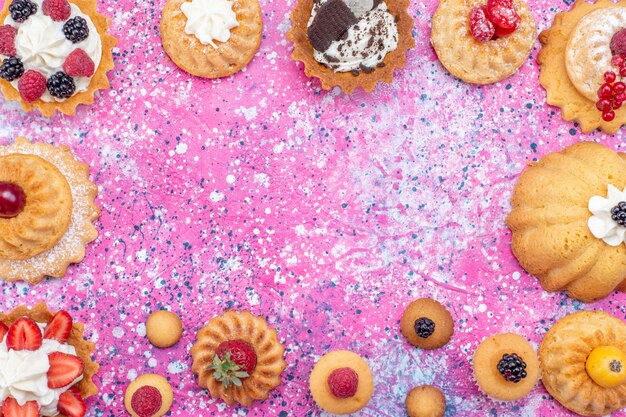 Draufsicht auf gebackene leckere Kuchen mit Sahne zusammen mit verschiedenen Beeren auf Licht