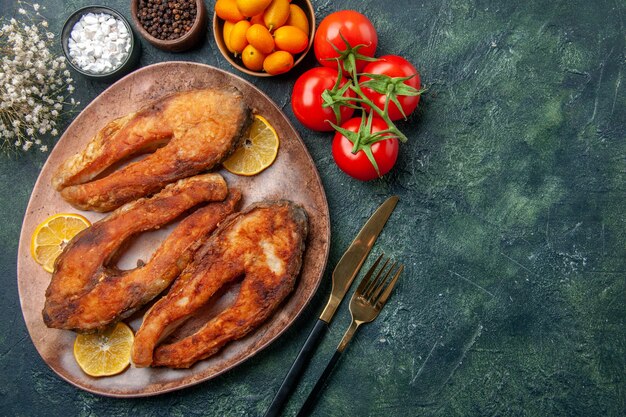 Draufsicht auf gebratene Fische und Zitronenscheiben auf einem braunen Teller Tomaten Kumquats auf Mischfarbtabelle mit freiem Raum