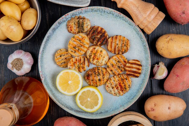 Draufsicht auf gebratene gekräuselte Kartoffelscheiben und Zitronenscheiben in Platte mit ganzem Butterknoblauch auf Holzoberfläche