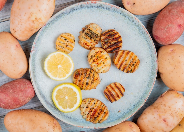 Kostenloses Foto draufsicht auf gebratene kartoffelscheiben und zitronenscheiben in platte mit weißen und roten kartoffeln herum auf holz