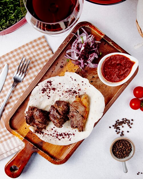 Draufsicht auf gebratenes Fleisch mit roten Zwiebeln auf einem Holzbrett